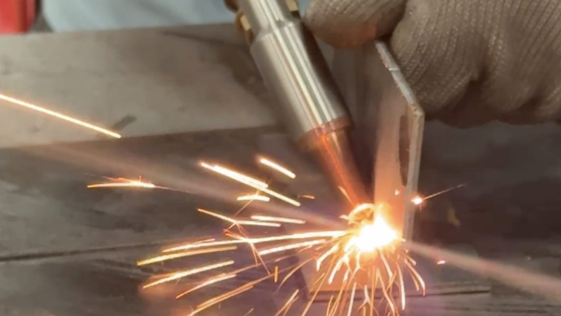 Welder laying a bead on a steel bracket, sparks flying