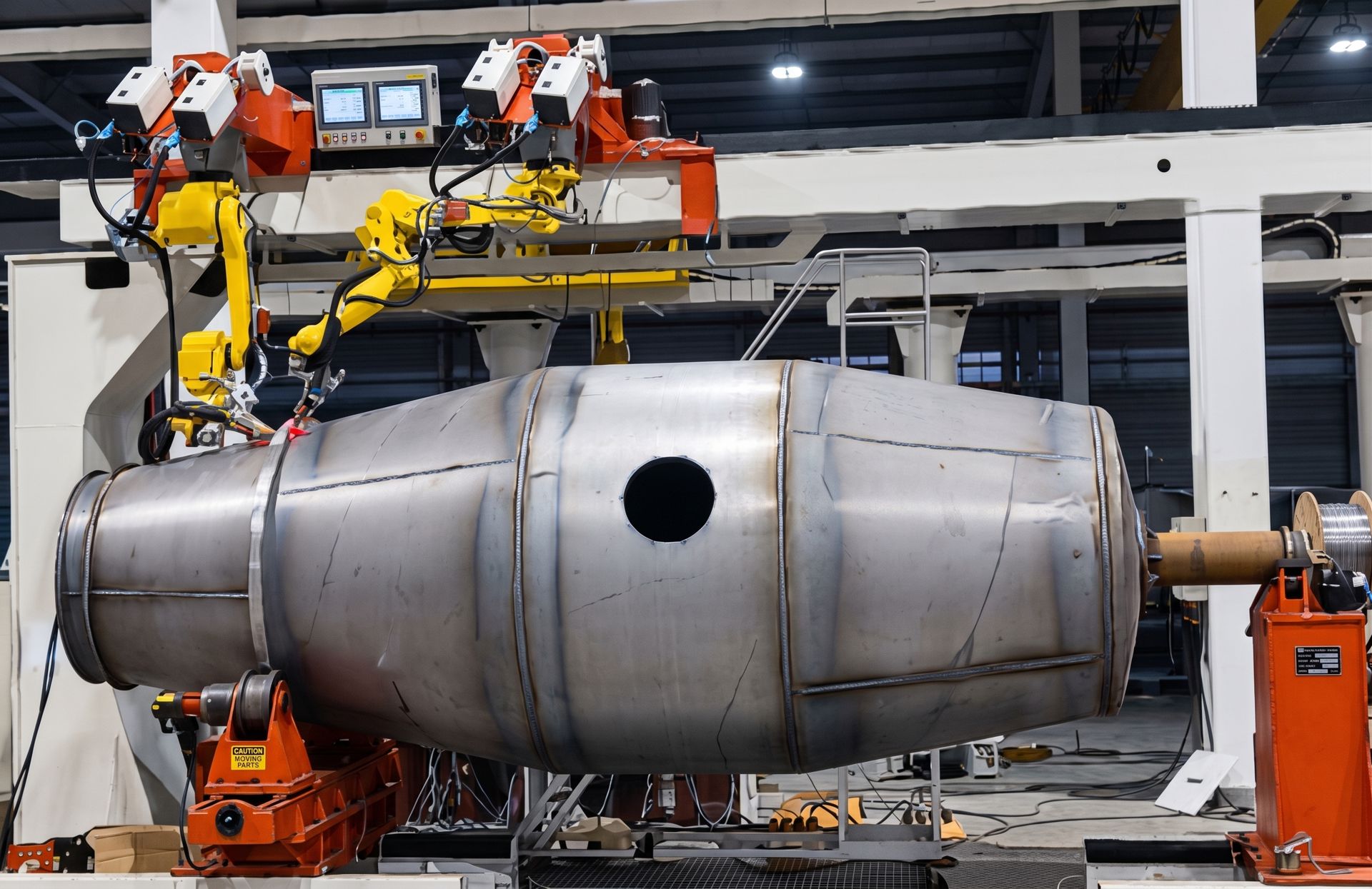 Two robotic welding arms joining a large fabricated cylindrical steel vessel