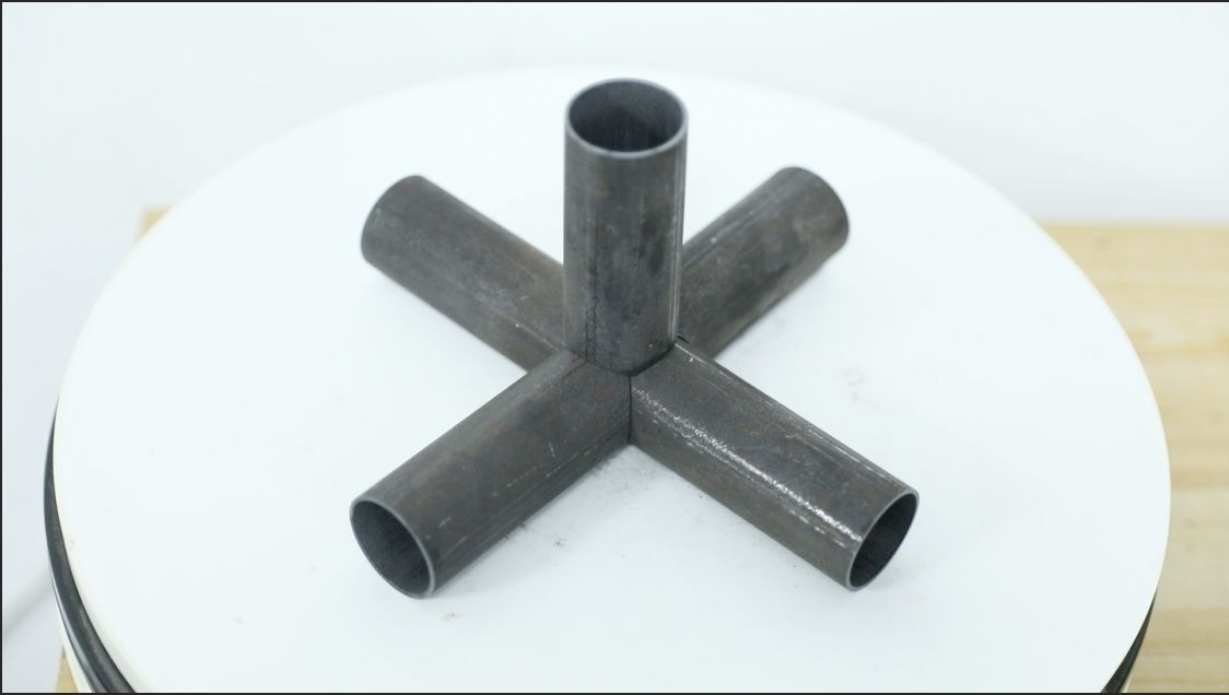 Fabricated five-way steel tube joint displayed on a white turntable